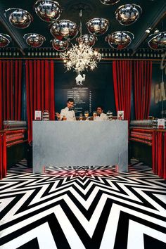 a man sitting at a counter in front of red curtains and chrome balls hanging from the ceiling