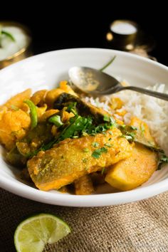 a white bowl filled with rice and curry next to a lime wedge on the side