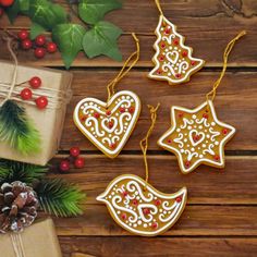 three decorated christmas cookies next to presents on a wooden table with holly and pine cones