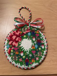 a cross stitch ornament hanging on a wooden table with a red and green ribbon