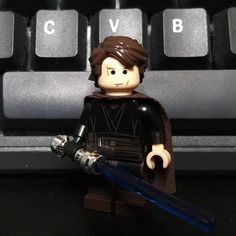 a lego star wars character holding a blue light saber in front of a computer keyboard