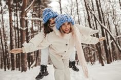 two girls are playing in the snow with their arms around each other and one girl is wearing a blue knitted hat