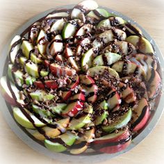 apple nachos with chocolate topping in a glass bowl on top of a wooden table