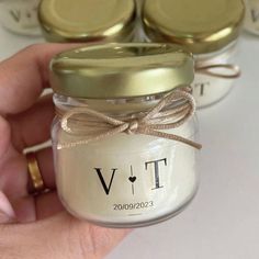 a person holding a jar with two gold lids and a bow on it's ribbon