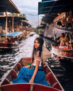 a woman in a blue skirt is sitting in a boat on the water with other boats