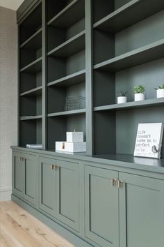 an empty bookcase with green cabinets and white vases on the top, in front of a wooden floor