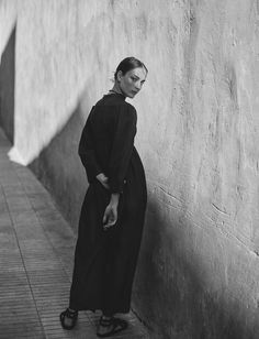 a woman leaning against a wall with her hand on her hip and looking down at the ground