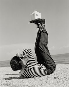 a man laying on the beach with his feet in the air while holding a kite above his head