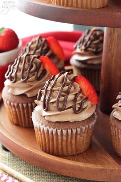 some cupcakes with chocolate frosting and strawberries on top are sitting on a wooden platter