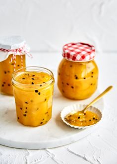 two jars filled with jam sitting on top of a white plate next to a spoon