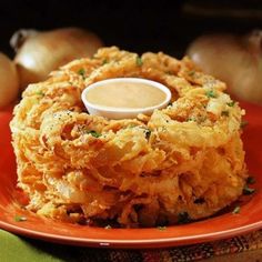 an orange plate topped with onion rings covered in sauce and garnished with parsley