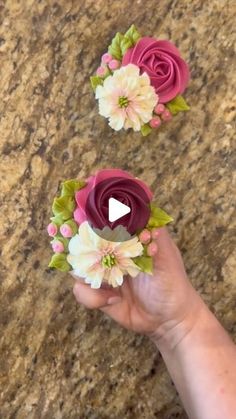 two fake flowers are being held up by someone's hand on a granite surface