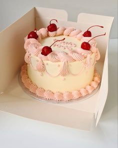 a white cake with pink frosting and cherries on top in a cardboard box