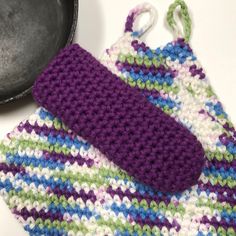 two crocheted pot holders sitting next to a black pan on top of a table