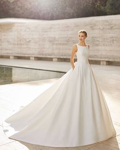 a woman in a white wedding dress standing by a pool with her hands on her hips