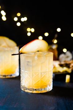 two glasses filled with an apple cider on top of a blue table covered in lights