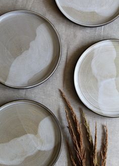 three white plates sitting on top of a table covered in dried grass next to each other