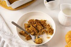 a white bowl filled with granola next to a cup of milk and two pumpkins