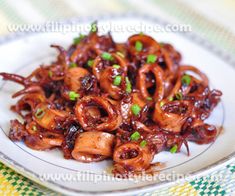 an octopus dish is served on a white plate with green onions and scallions