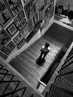 a black and white photo of a person standing on the stairs in front of a wall covered with pictures