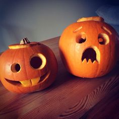 two carved pumpkins sitting on top of a wooden table with their faces cut out