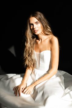 a beautiful woman sitting on top of a bed wearing a white dress and posing for the camera