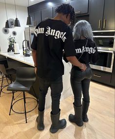 two people standing in a kitchen wearing matching black shirts and pants with white writing on them