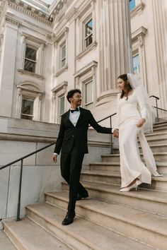 a bride and groom walking down the stairs in front of an old building holding hands