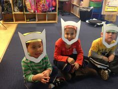 three children sitting on the floor wearing paper hats with cat's head cutouts