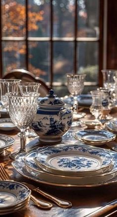 a dining room table set with blue and white china plates, silverware and glasses