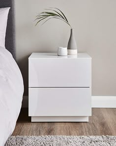 a white nightstand sitting on top of a wooden floor next to a bed