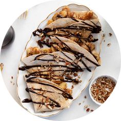 a white plate topped with sliced bananas covered in chocolate sauce and nuts next to a bowl of granola