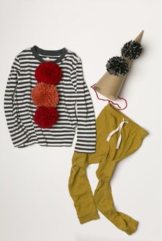 a child's outfit and hat are laid out on a white surface, including a striped sweater with red pom - poms