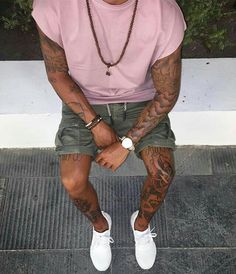 a man sitting on the ground with tattoos on his arms and legs, wearing white sneakers