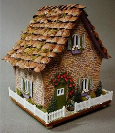 a doll house with a fence and flowers on the roof