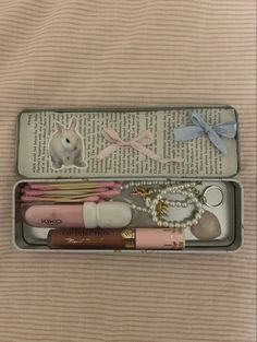 an open box containing various items such as lipstick, bracelets and hair clips on top of a bed