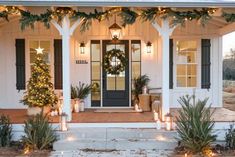 a white house decorated for christmas with wreaths and candles on the front porch,