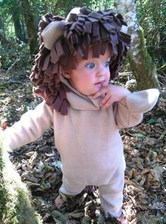 a small child wearing a lion costume in the woods with leaves on it's head