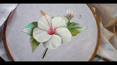 a close up of a white flower on a embroidery hoop with green leaves and flowers