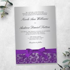 a purple and silver wedding card with a bow on the front, sitting next to some greenery