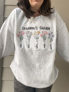 "EMBROIDERED CUSTOM GARDEN APPAREL ♡ Heavy Blend Crewneck Sweatshirt - Unisex ♡ Personalized Mom/Grandma Garden Crewneck ♡ 50/50 Cotton/Polyester ♡ Made in the U.S. ♡ Sample photo is \"Ash\"; Size: \"L\" IMPORTANT NOTICE: Crewnecks now have a paper like stabilizer that appears on the inside. This helps with increasing quality and ensure a longer lasting design on the sweatshirts. NOTE: Flower colors will remain the same. You may alter the text thread color. NOTE: INVENTORY IS CONSTANTLY CHANGING Grandma Embroidered Sweatshirt, Grandma Embroidery, Grandma Garden, Mom Crewneck, Grandma's Garden, Grandmas Garden, Flower Colors, Gardening Outfit, Personalized Grandma