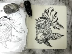 two drawings of fish on paper next to a pen and ink drawing pad with markers