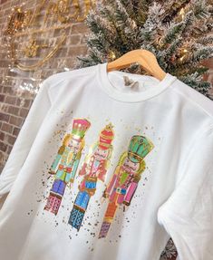 a white t - shirt with three nutcrackers painted on it sitting next to a christmas tree