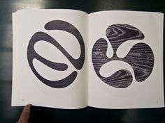 an open book with two black and white designs on the pages, in front of a person's hand