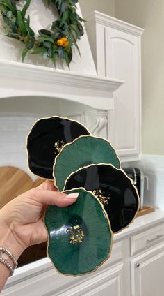 a person holding three black and green plates in front of a white fireplace mantel