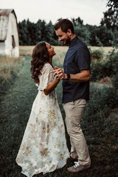 a man and woman are standing in the grass with their arms around each other as they look at each other