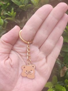 a hand holding a gold colored teddy bear keychain in it's palm