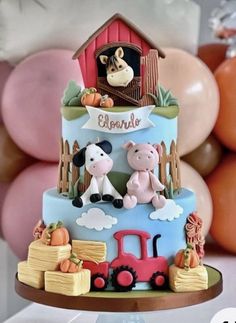 a three tiered cake decorated with farm animals and farm scene on the top, along with balloons in the background