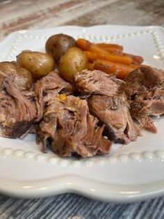 a white plate topped with meat, potatoes and carrots on top of a wooden table