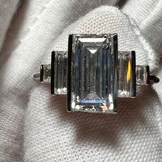 an emerald cut diamond ring sitting on top of a white cloth